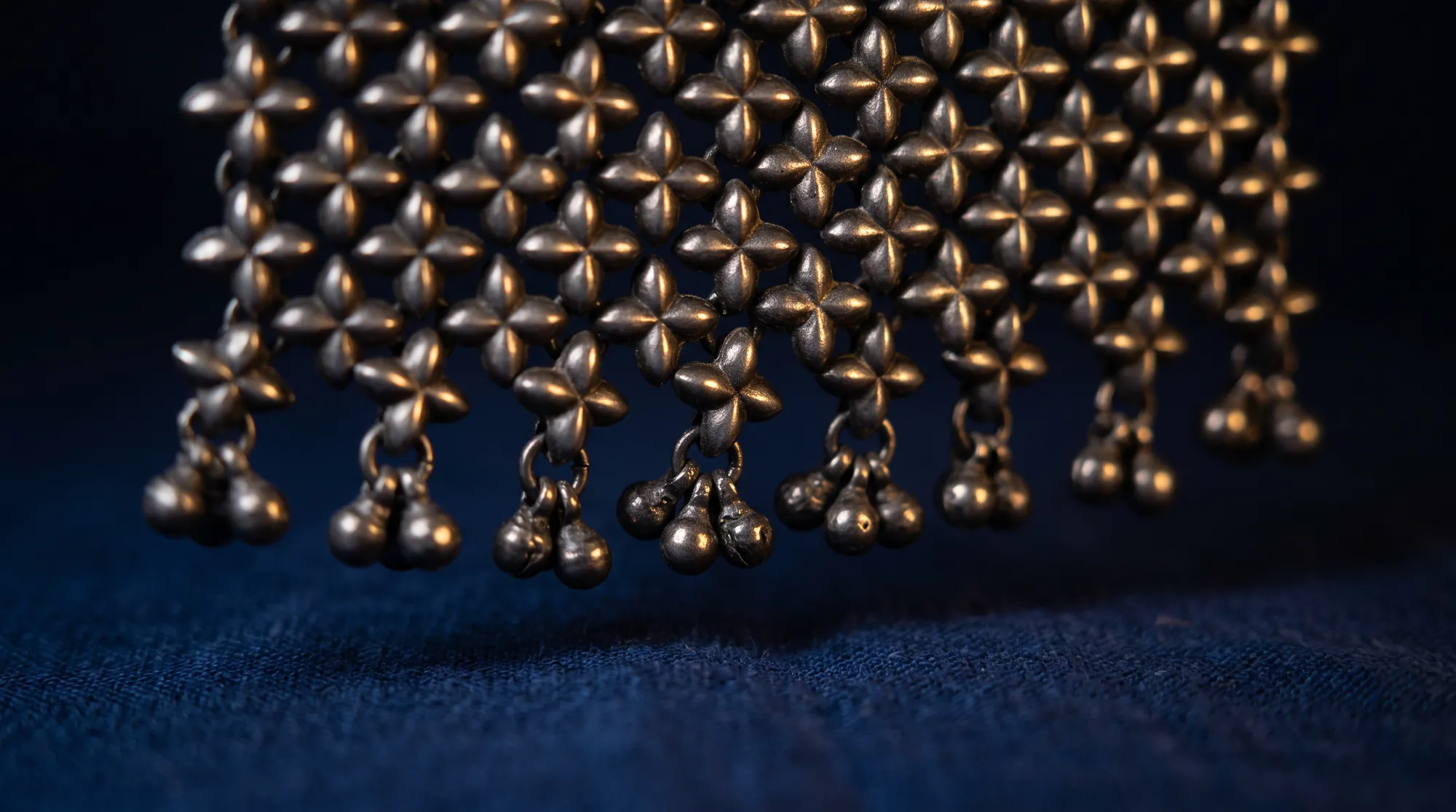 Close-up of a silver fringe of four-petal flower links ending in tiny ghungroo bells