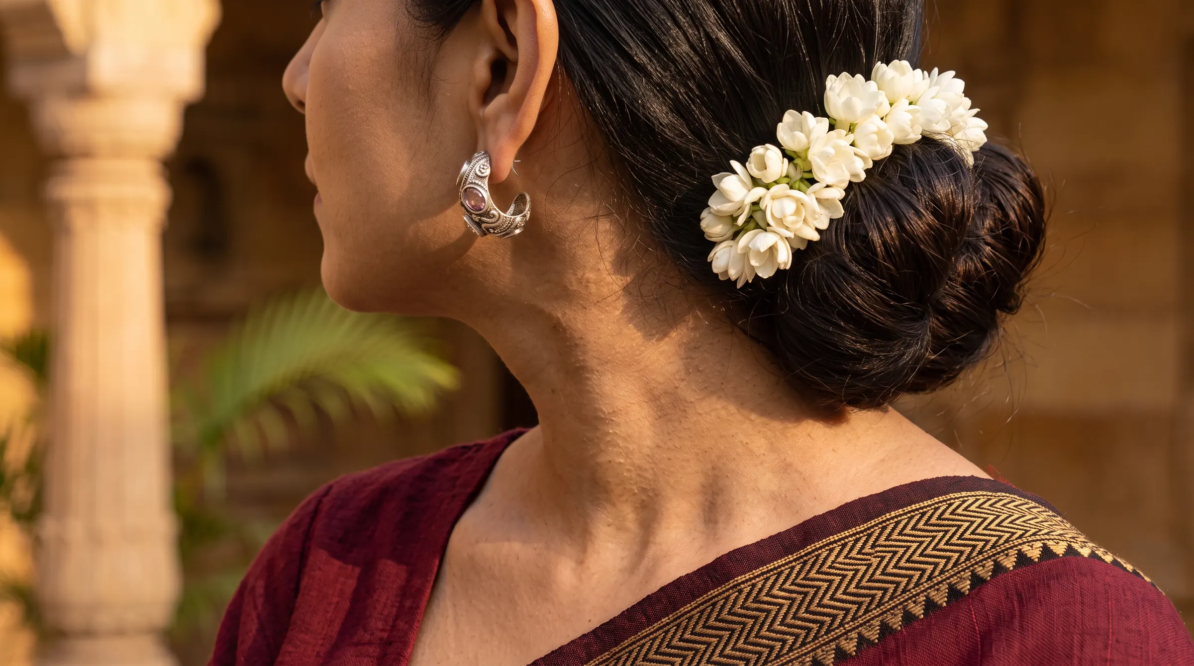 A woman in a maroon handloom saree wearing a silver earring, jasmine in her hair