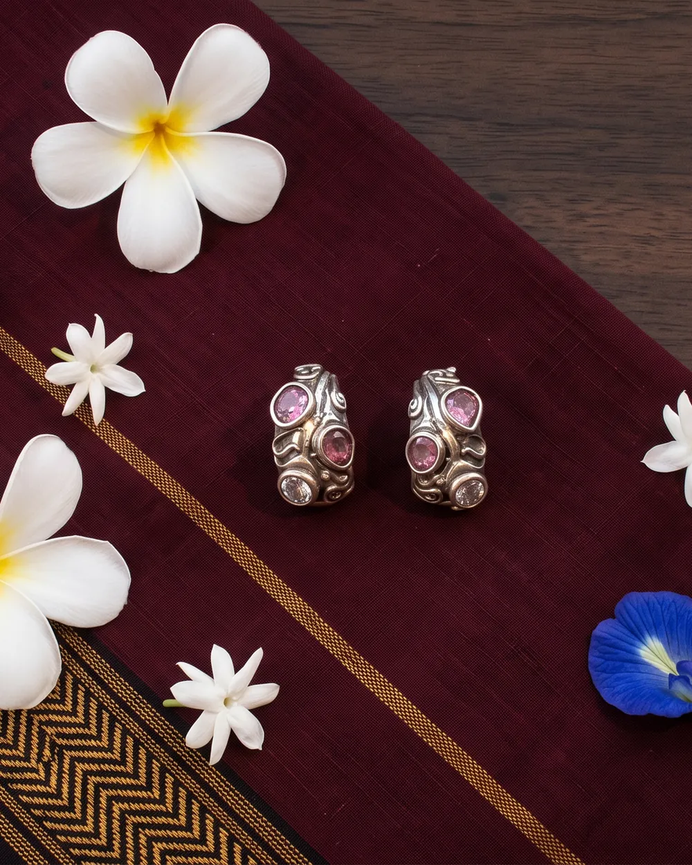Silver earrings with pink stones on maroon handloom with frangipani, jasmine and a butterfly-pea flower